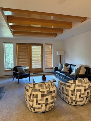 A modern living room with a black leather sofa, two patterned ottomans, a coffee table, and a lamp. - True Ski-in Ski-out at Solitude - with pool and hot tub (Brighton)
