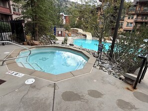A swimming pool with a slide, surrounded by trees and a stone border. - True Ski-in Ski-out at Solitude - with pool and hot tub (Brighton)