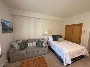 Quarto com cama, sofá, abajur e porta.