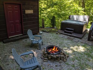 Une cabane en bois avec un foyer, deux fauteuils Adirondack et un bain à remous.