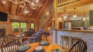 Un intérieur de chalet chaleureux comprenant un coin repas, des fauteuils inclinables en cuir, une cheminée et une cuisine agrémentée d’éléments en pierre.