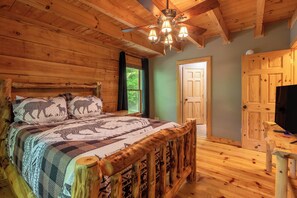 Une chambre dans une cabane en bois, avec un lit, un ventilateur de plafond, une porte et un téléviseur.