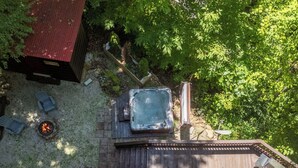 Un bain à remous sur une terrasse en bois, avec un foyer, entouré de verdure et délimité par une clôture en bois.