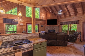 A cabin interior with a stone fireplace, leather recliners, a kitchen with a gas stove, and large windows. - Nantahala Adventures- Hot tub- Firepit- Foosball Table (Bryson City)