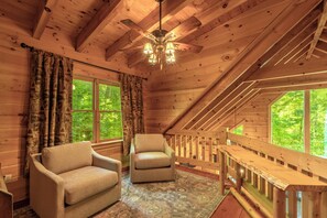 A cozy cabin interior with a wooden ceiling, two windows with curtains, a sofa, a chair, and a patterned rug. - Nantahala Adventures- Hot tub- Firepit- Foosball Table (Bryson City)