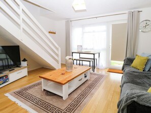 Ein Wohnzimmer mit Fernseher, Couch, Holz-Couchtisch, einer Treppe und einem Essbereich.