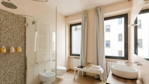 A modern bathroom with a glass-enclosed shower, a bidet, a toilet, and a vanity with a large sink. - Numa Rome Via Veneto (Roma)