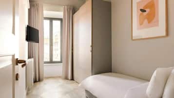 Habitación de hotel con cama, televisor, puerta que da a un balcón y un cuadro abstracto enmarcado en la pared.