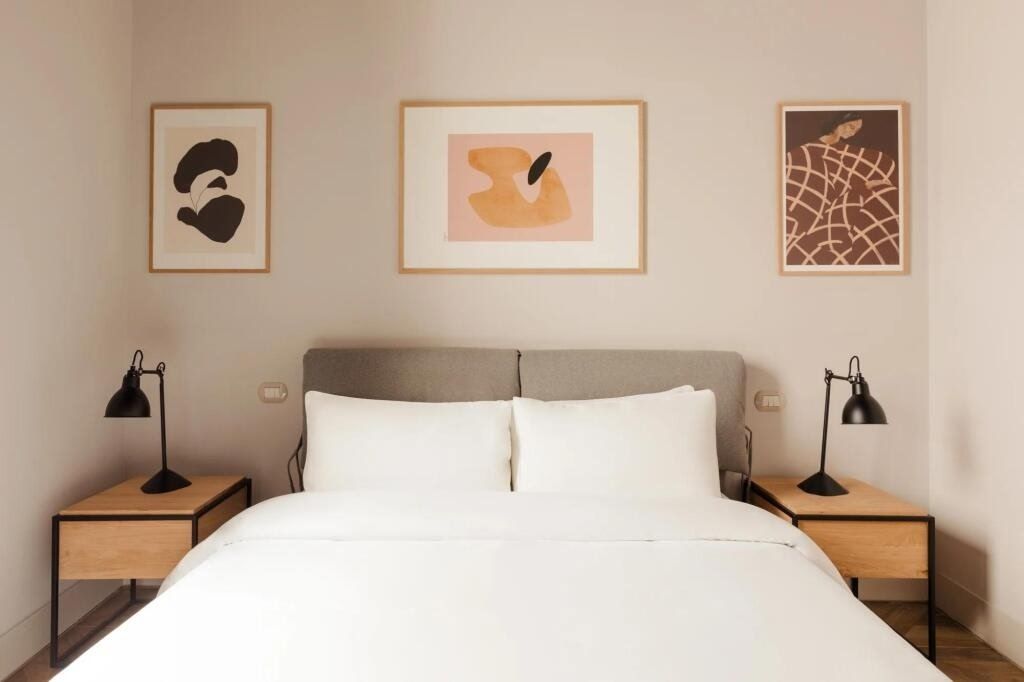 Ein Hotelzimmer mit einem Bett, zwei Nachttischen und drei gerahmten Kunstwerken an der Wand.
