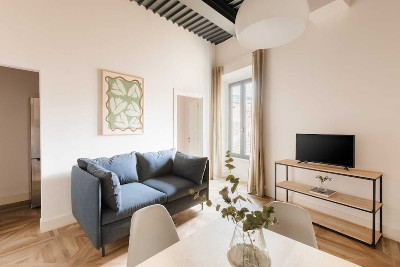 A modern living room with a sofa, a dining table, and a TV on a wooden stand.