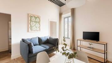 A modern living room with a sofa, a dining table, and a TV on a wooden stand.