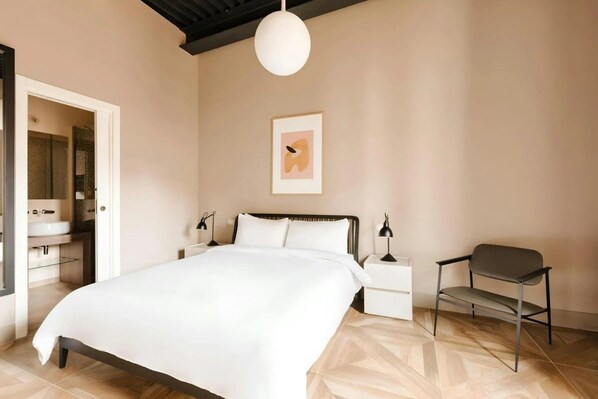 A bedroom with a bed, bedside tables, a chair, a hanging light fixture, and a framed picture on the wall.