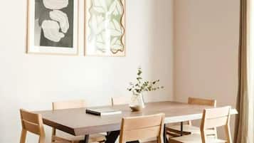 Un comedor con una mesa y sillas de madera, una obra de arte enmarcada en la pared y una lámpara colgante.