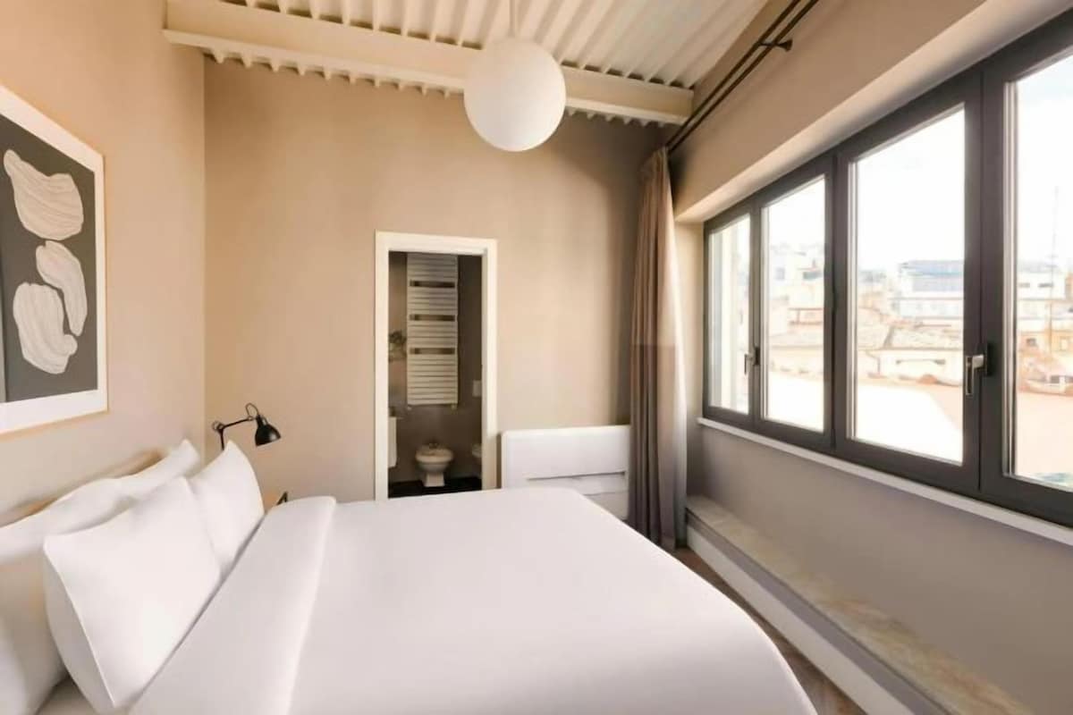 A hotel room with a large bed, a window with a view, and a door leading to a bathroom.