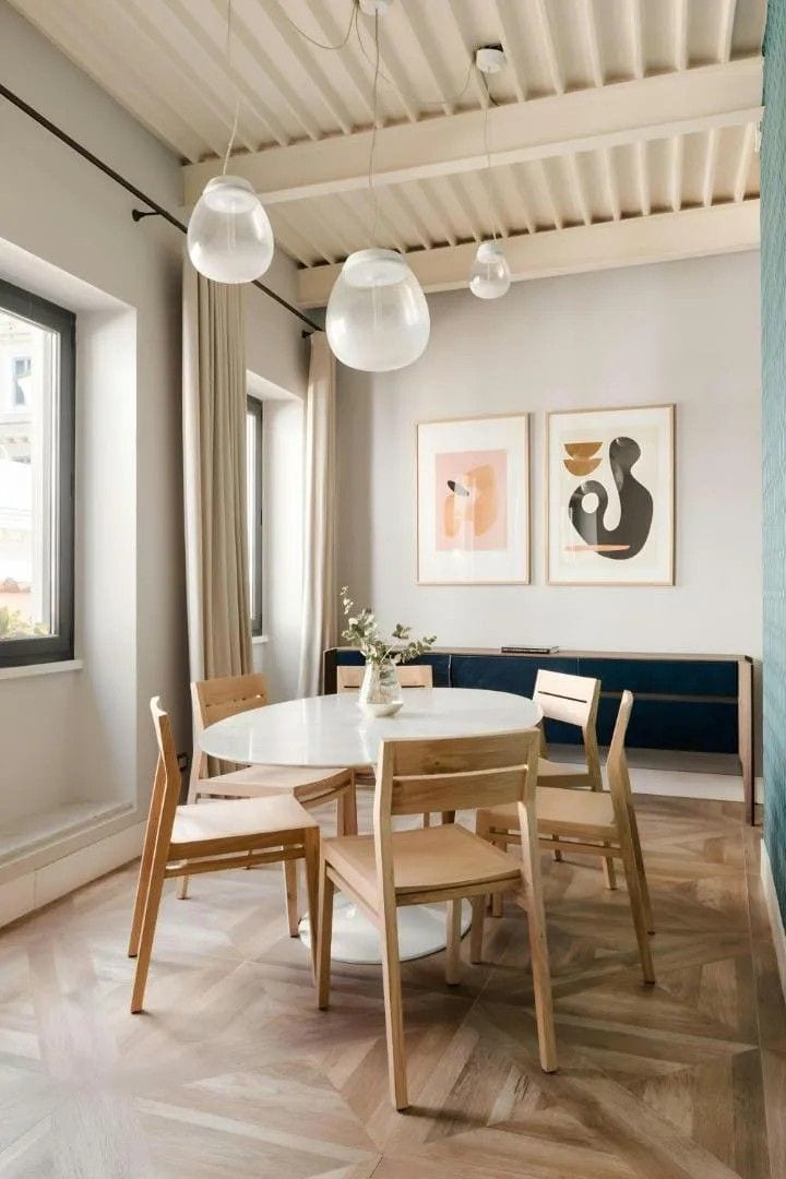 Zona pranzo con tavolo rotondo, sedie in legno, illuminazione a sospensione e opere d'arte alle pareti.