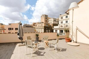 Eine Dachterrasse mit Gartenmöbeln, einer Lampe und Topfpflanzen.