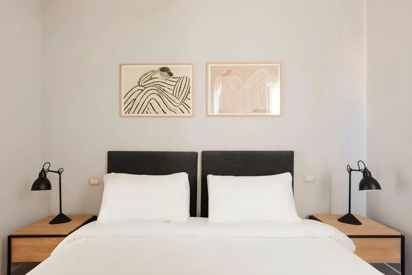 A double bed with two nightstands, each with a lamp, and two framed artworks on the wall.