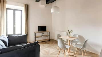 Una sala de estar moderna con un sofá, un televisor sobre un mueble de madera, una mesa de comedor con sillas y una lámpara colgante.