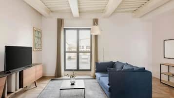 Una sala de estar moderna con un televisor de pantalla plana, un sofá azul oscuro, una mesa de centro y un amplio ventanal con cortinas.