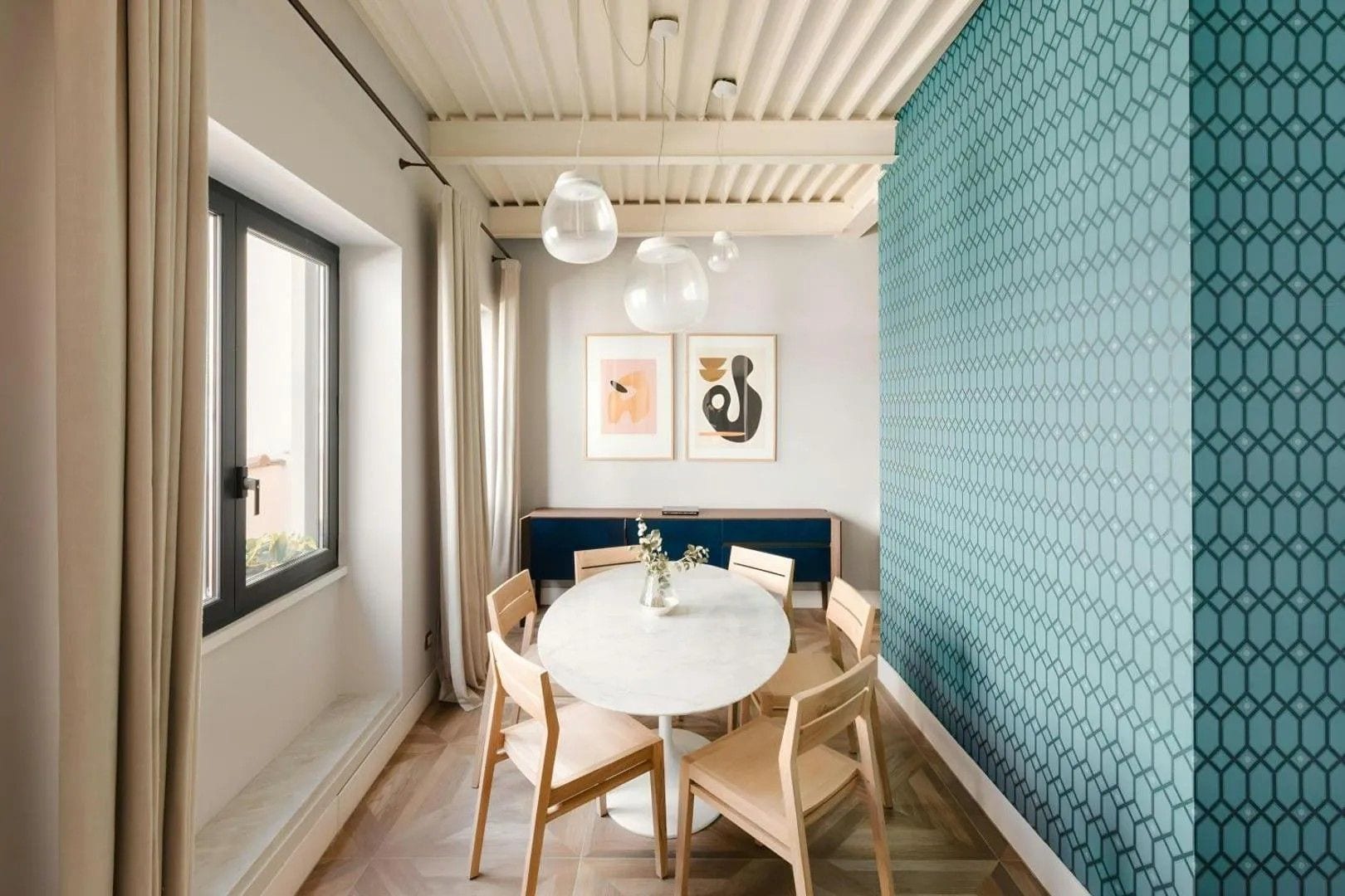 Una zona pranzo con un tavolo rotondo, sedie in legno, una panca imbottita blu e lampade a sospensione.