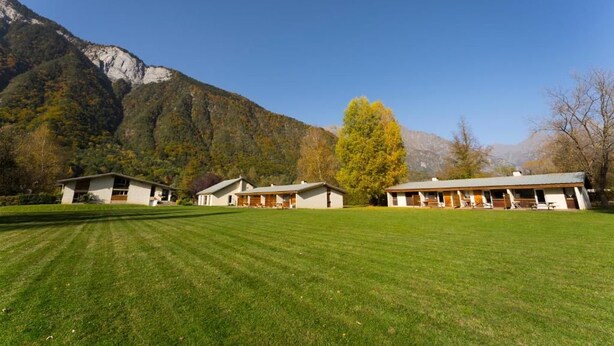 A hotel with multiple buildings, a well-maintained lawn, and mountains in the background. - Gîtes Le grand Renaud (Le Bourg-d'Oisans)