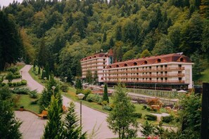 A multi-story hotel with a central courtyard, surrounded by lush greenery and a forested hillside.