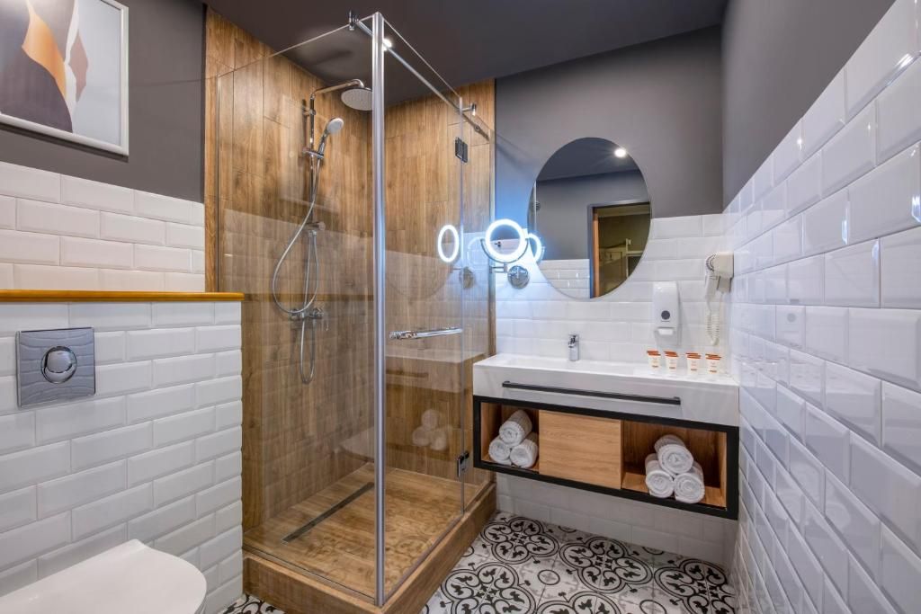 A modern bathroom with a glass-enclosed shower, white tiled walls, a wooden vanity, and a mirror with lights.