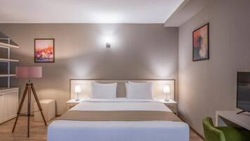 A hotel room with a large bed, bedside lamps, a desk with a television, and a tripod lamp.