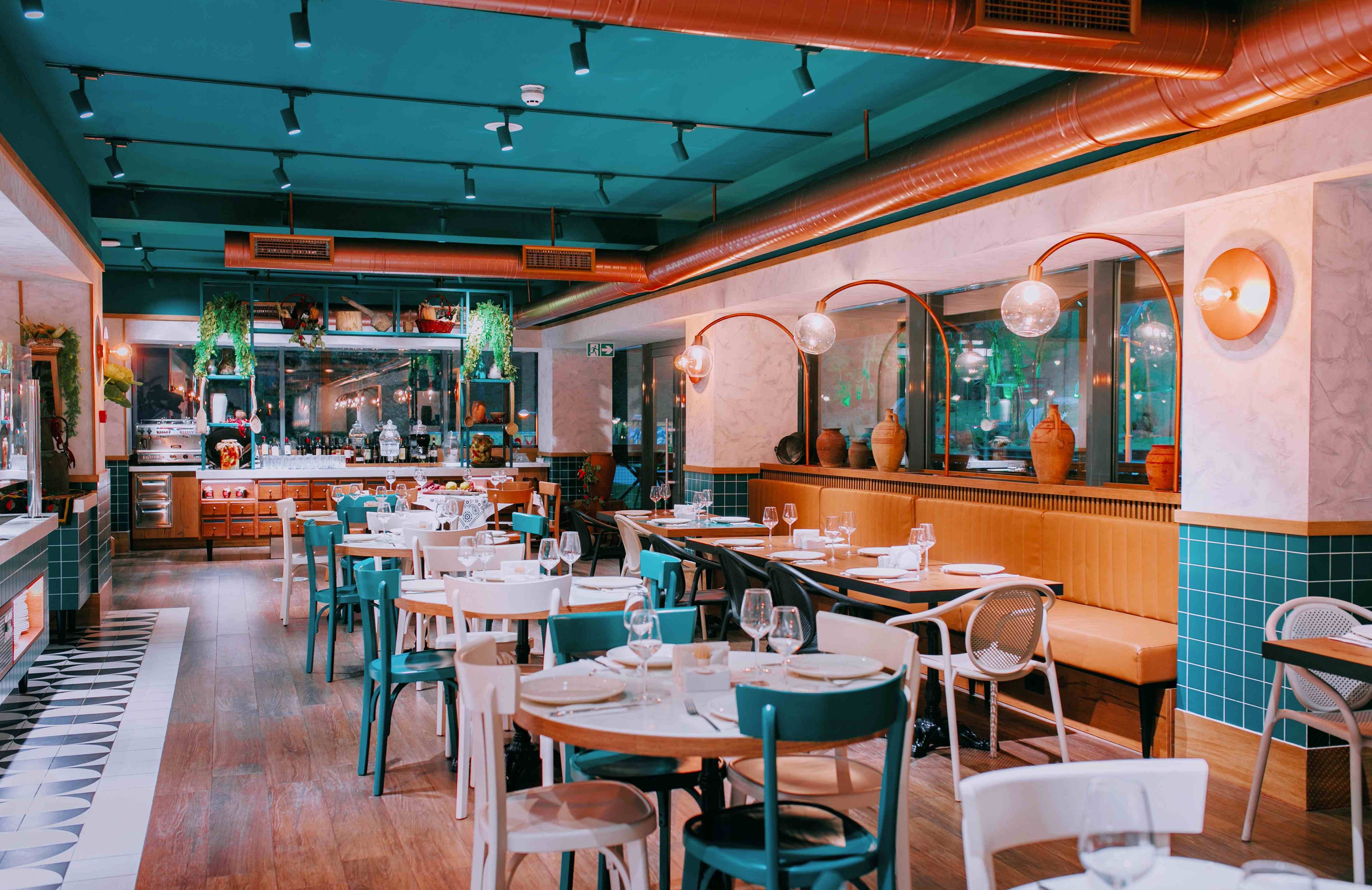 L’intérieur d’un restaurant, avec plusieurs tables et chaises, un bar et une cuisine en arrière-plan.