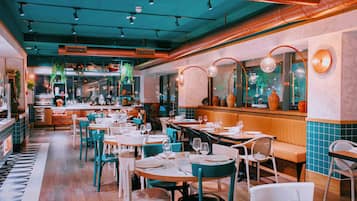 L’intérieur d’un restaurant, avec plusieurs tables et chaises, un bar et une cuisine en arrière-plan.