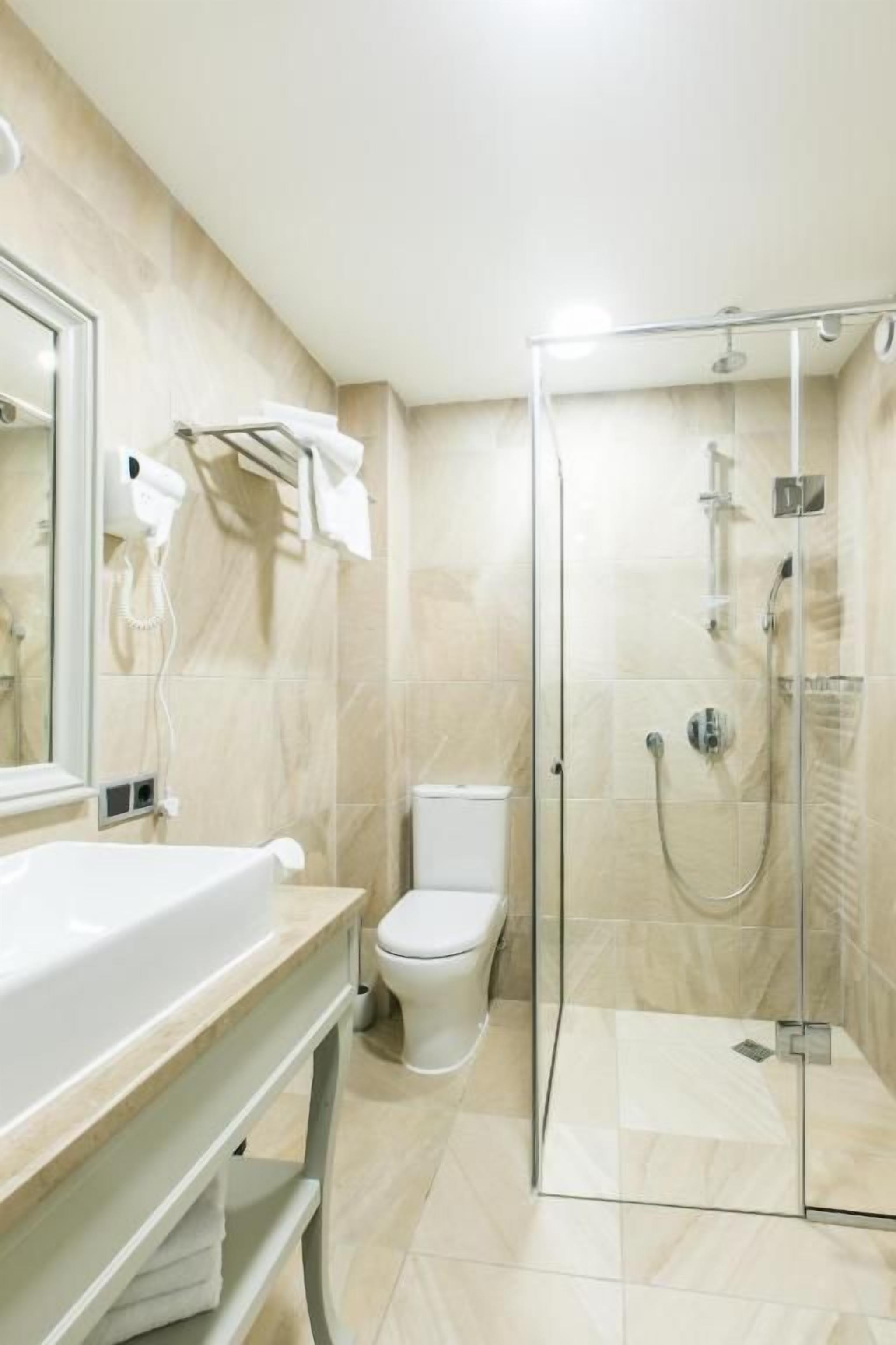 Un baño moderno con ducha envuelta en vidrio, un lavamanos blanco y un inodoro.
