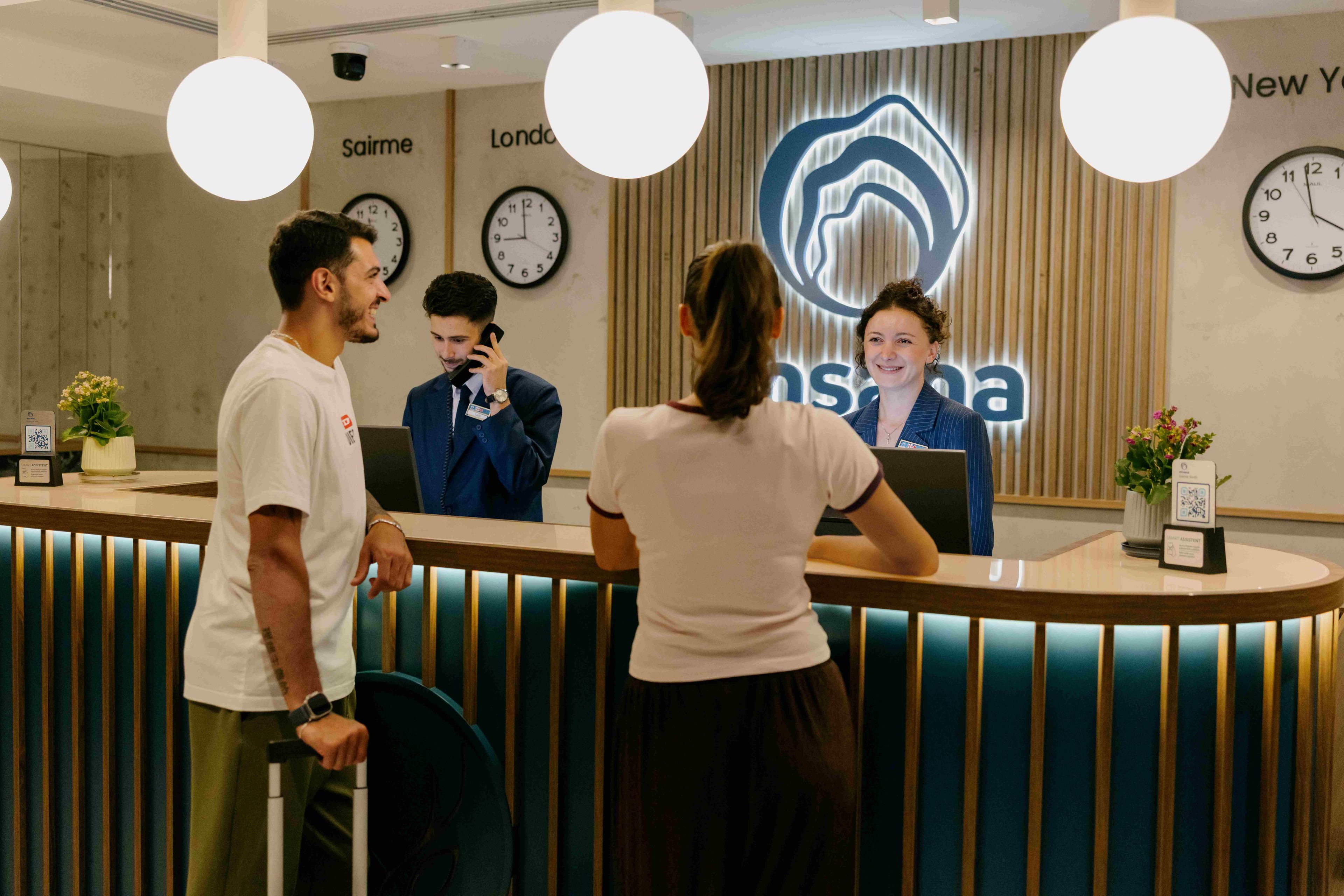 Una recepción de diseño moderno, con un reloj, una pantalla digital y un letrero con el nombre del hotel.
