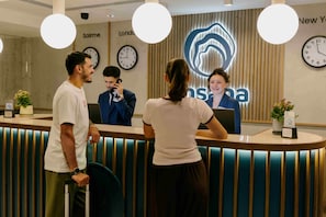 A reception desk with a modern design, featuring a clock, a digital display, and a sign with the hotel's name.