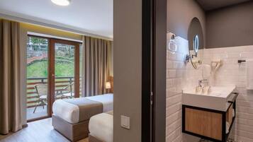 Habitación de hotel con balcón, cama, baño con lavamanos y espejo, y vista a zonas verdes.