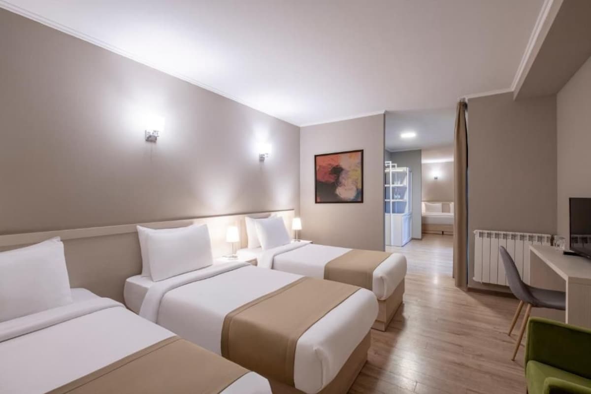 A hotel room with three beds, a desk, and a chair.