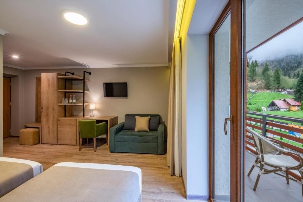 Quarto de hotel com varanda, escrivaninha, sofá e televisão.