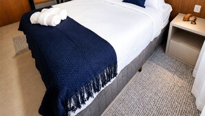 Ett hotellrum med en säng, ett nattduksbord, en vägghylla och en dörr.