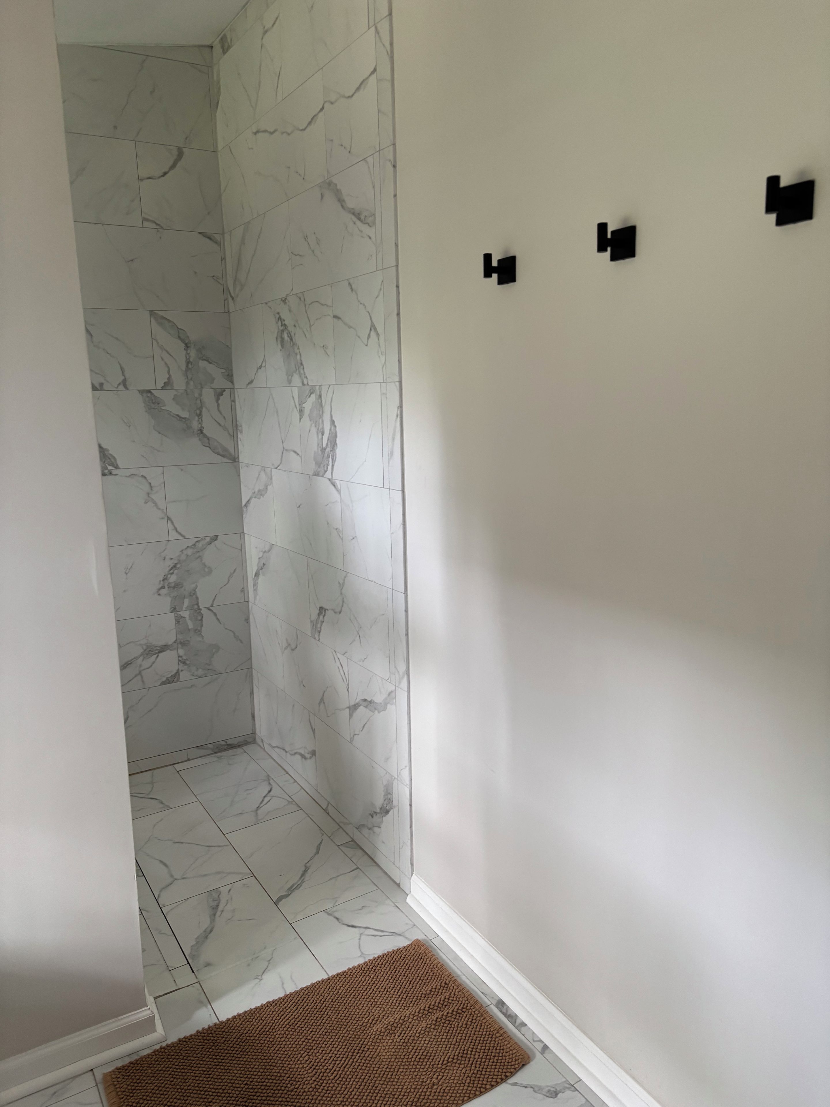 A bathroom with white marble tiles, a brown rug, and a white wall with three black rectangular objects.