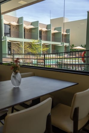 A dining area with a table and chairs, a vase with flowers, and a view of a multi-story building with balconies. - Essence Paradise Pousada Charme (Bonito)