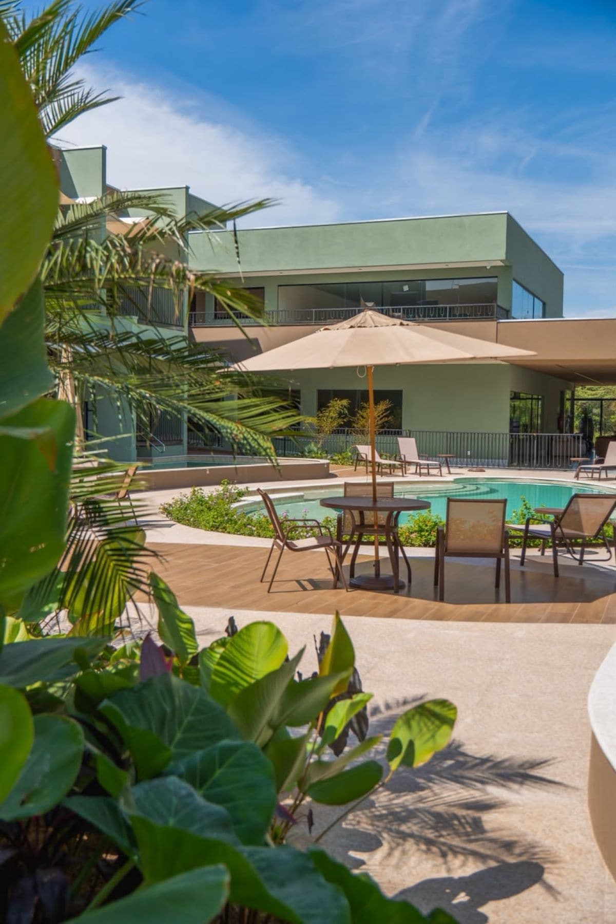 A modern building with a pool area, including lounge chairs and a table with an umbrella.