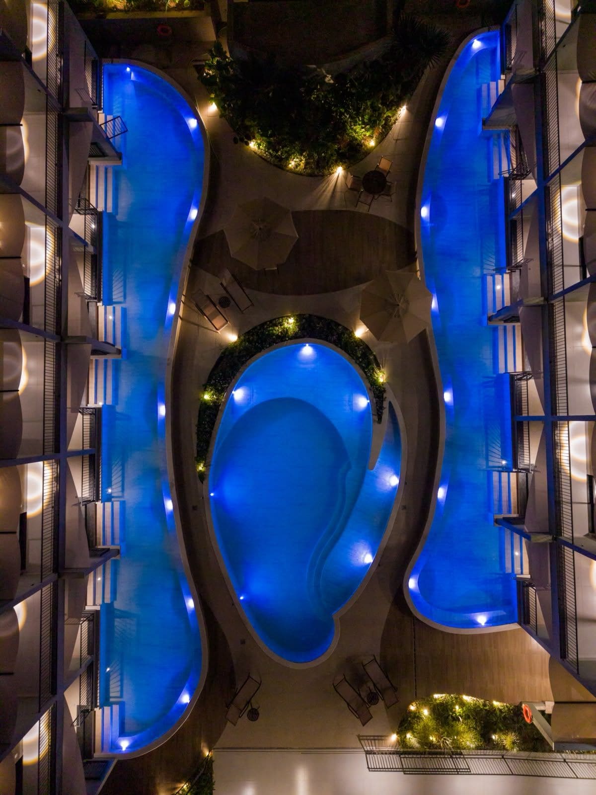 A modern hotel with a central swimming pool, multiple balconies, and outdoor seating areas.