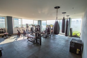 Ein Fitnessstudio mit verschiedenen Trainingsgeräten, großen Fenstern und Blick ins Freie.