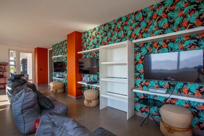 Ein modernes Wohnzimmer mit großem Flachbildfernseher, eingebauten Regalen und lebhaftem, blattmusterigem Wandpapier.