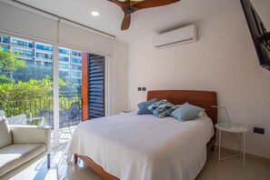 Ein Schlafzimmer mit einem großen Bett, einem Deckenventilator, einer Klimaanlage, einem Nachttisch und Blick auf einen Balkon mit Gartenmöbeln.