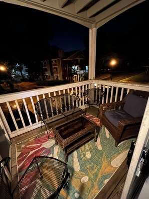 Un balcon agrémenté de meubles en osier, d’un tapis à motifs et offrant une vue sur les bâtiments illuminés la nuit.