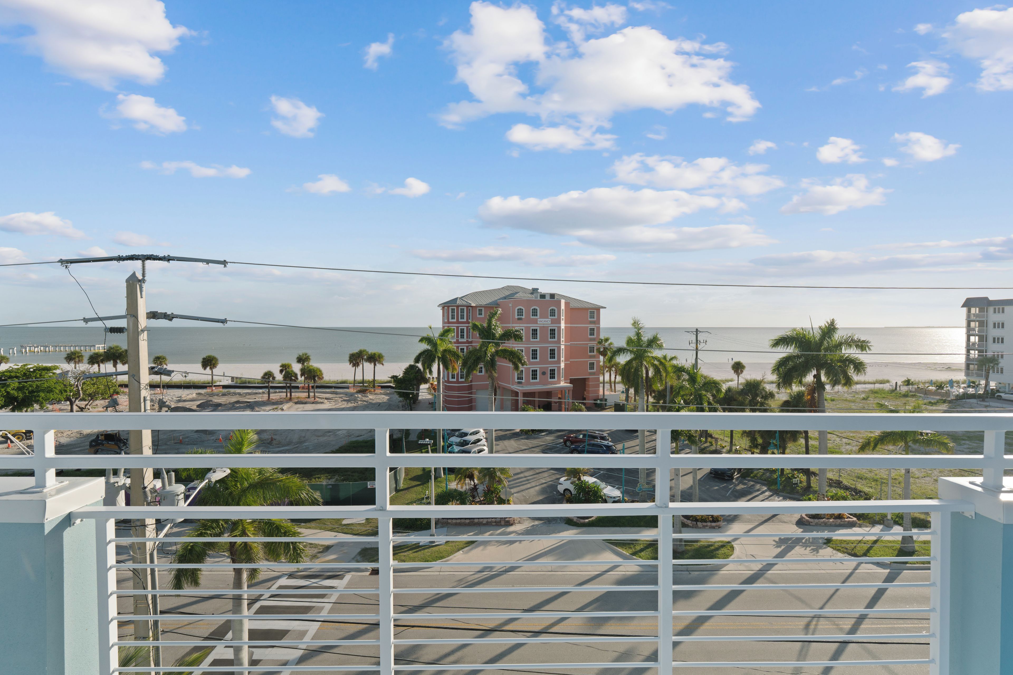 A beachfront hotel with a view of the ocean, a parking lot, and a pedestrian walkway.
