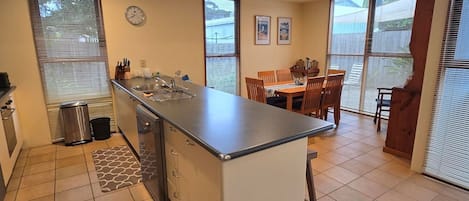 A compact kitchen with a central island, a dining area with a wooden table and chairs, and a clock on the wall.