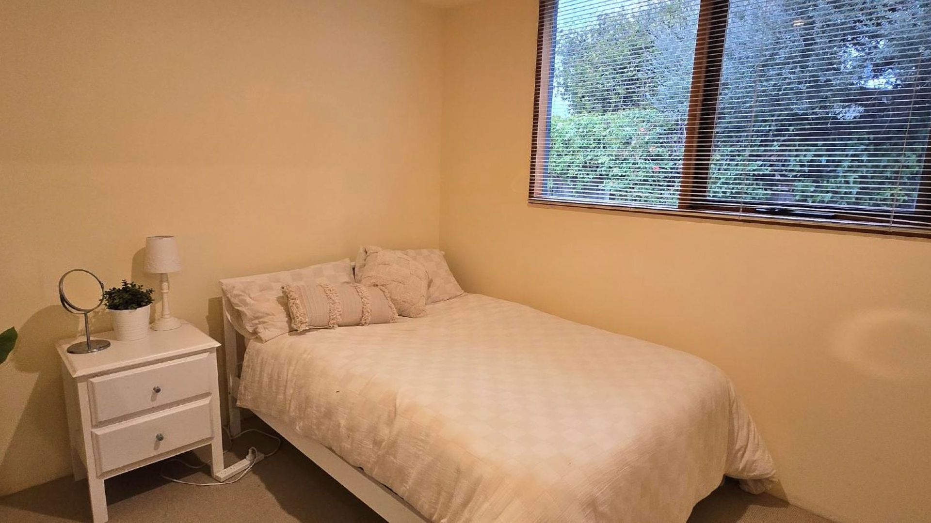A bedroom with a single bed, a bedside table with a lamp, and a window with blinds.