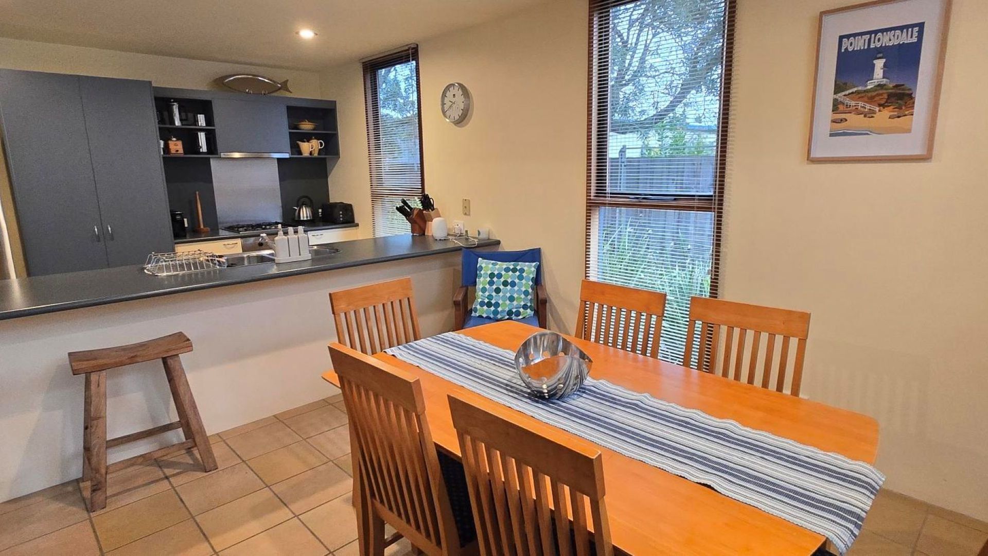 A dining area with a wooden table, four chairs, a striped table runner, and a decorative bowl.