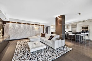 A modern living room with a white sofa, a coffee table, and a kitchen area with bar stools. - The Wavefront | Gulf-front Executive Residence (St. Pete Beach)